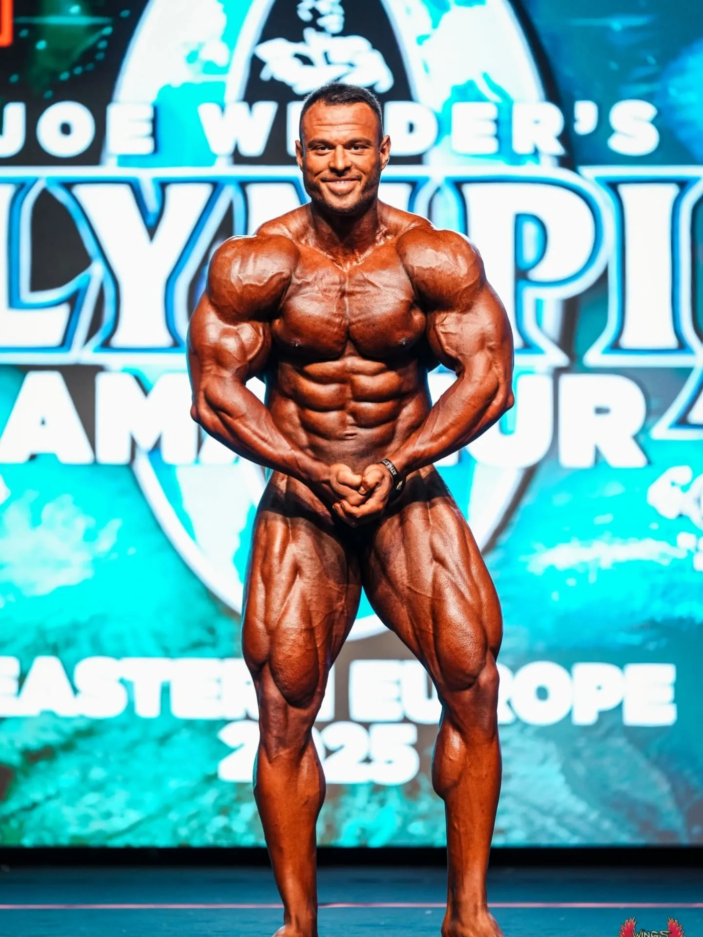 Bozhidar Pecakovski front double biceps pose on stage at Olympia Amateur Eastern Europe 2025